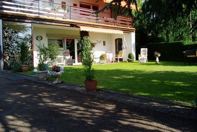 Ein gemütliches Haus mit einem gepflegten Garten. Auf der Terrasse stehen Möbel und Pflanzen in Töpfen.