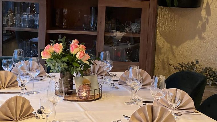 Ein elegant gedeckter Tisch mit Stoffservietten und Glasgeschirr. In der Mitte steht ein Blumenarrangement mit rosafarbenen Rosen.