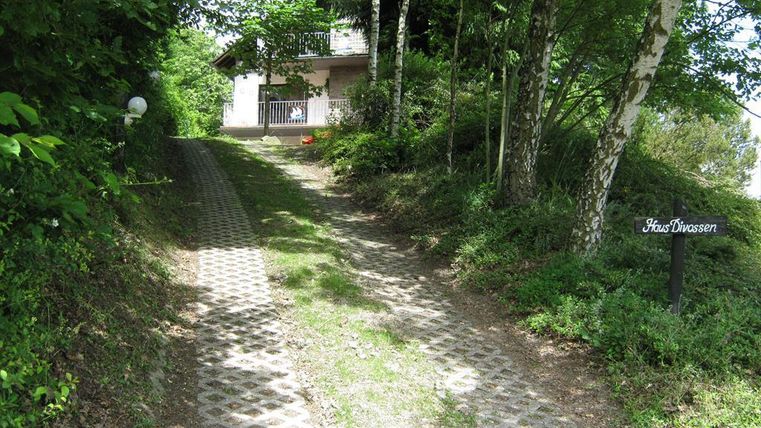 Ein befestigter Weg führt zu einem Haus, umgeben von Bäumen und Grün. Ein Schild mit der Aufschrift "Haus Danner" ist sichtbar.