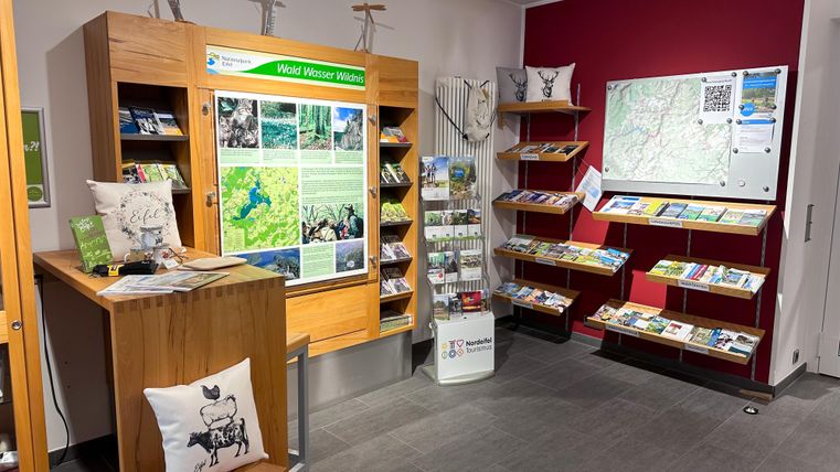 An information center with wooden shelves and brochures. A map hangs on the wall and there are inviting seating options.