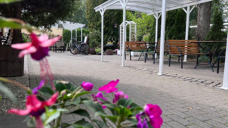 Een uitnodigende buitenruimte met zitgelegenheden en overdekte tafels. Kleurrijke bloemen op de voorgrond geven de plek een vrolijke sfeer.