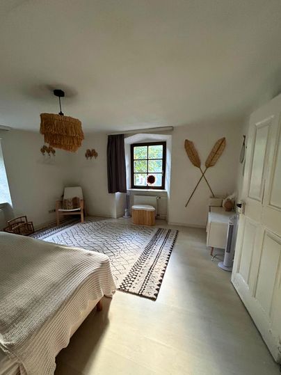 A bright bedroom with a large rug and decorative elements on the walls. The decor is simple and modern, with a window that lets in daylight.