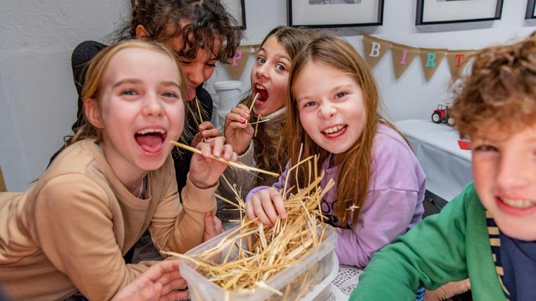 Eine Gruppe von fröhlichen Kindern lächelt und spielt zusammen. Sie halten Stäbe und arbeiten an einem kreativen Projekt.