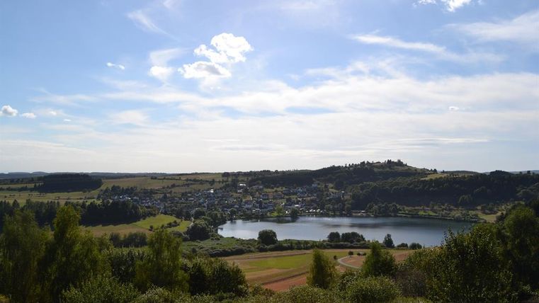 Eine malerische Landschaft mit einem ruhigen See und sanften Hügeln. Der Himmel ist klar und die Natur ist grün und üppig.