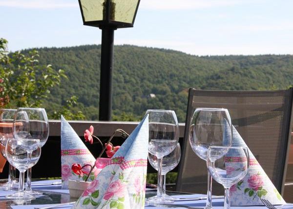 Ein schön gedeckter Tisch im Freien mit Weingläsern und dekorativen Servietten. Im Hintergrund ist eine grüne Hügel-Landschaft zu sehen.