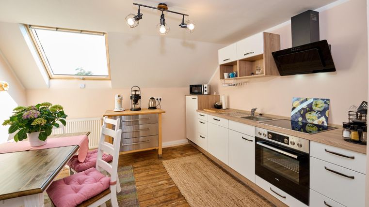A modern kitchen with white cabinets and wooden surfaces. The room is bright and welcoming, with a table and a beautiful flower.