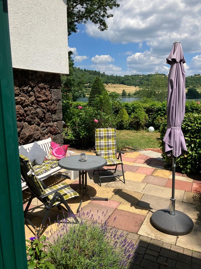 Ein einladender Außenbereich mit Gartenmöbeln und einem Sonnenschirm. Die Umgebung ist grün und bei schönem Wetter, ideal zum Entspannen.