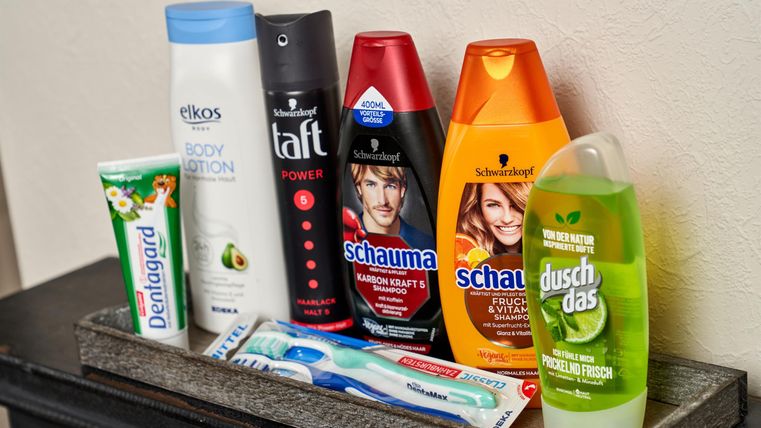 A range of personal care products is displayed on a shelf. These include shampoos, shower gel, toothpaste, and a toothbrush.