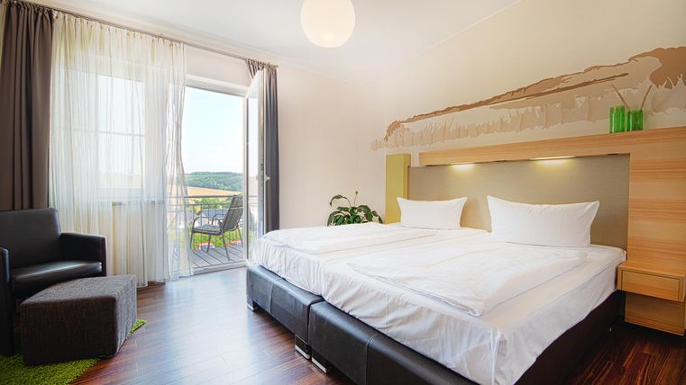 A modern hotel room with two single beds and bright curtains. The room has a balcony with a view outside and a cozy seating area.