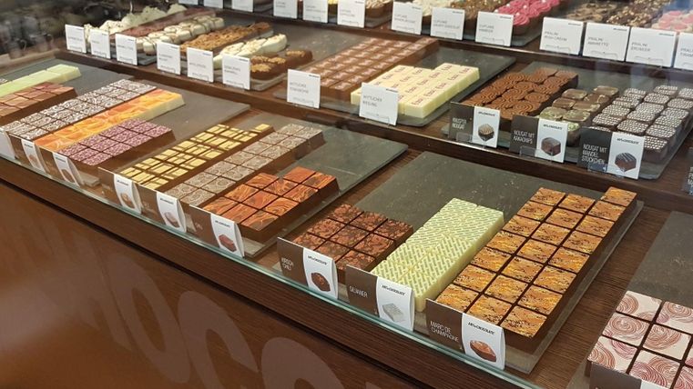 Eine Vitrine voller bunter Pralinen und Schokoladenstücken. Die verschiedenen Sorten sind ansprechend angeordnet und bieten eine Vielzahl von Geschmacksrichtungen.