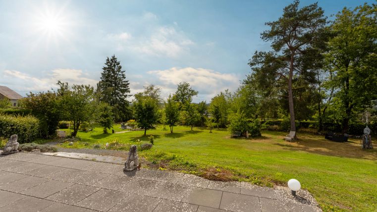 A beautiful garden with many trees and sunshine. The lawn is green and well-maintained.