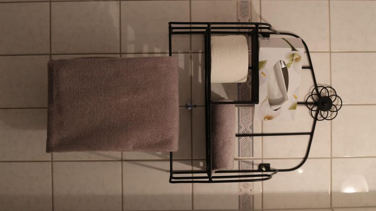 Ein modernes Badezimmermöbel mit einer schwarzen Metallstruktur und einer gepolsterten Sitzgelegenheit. Auf dem Möbel befinden sich Pflegeprodukte und Handtücher.