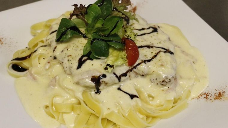 Een bord pasta met roomsaus, mager vlees en verse groenten. De garnering bestaat uit sla en cherrytomaten.