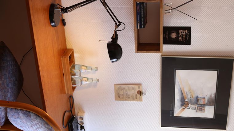 Ein gemütlicher Schreibtisch mit einer Schreibtischlampe und einer Holzablage. An der Wand hängen ein Kunstwerk und weitere dekorative Elemente.