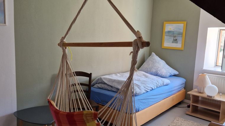 Een gezellige kamer met een hangstoel en een bed. De muren zijn in zachte kleuren geschilderd en er is een kleine tafel.