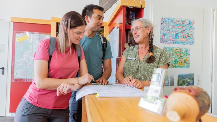 Een vriendelijk gesprek bij een balie. Twee gasten bekijken samen met een medewerker een plattegrond.