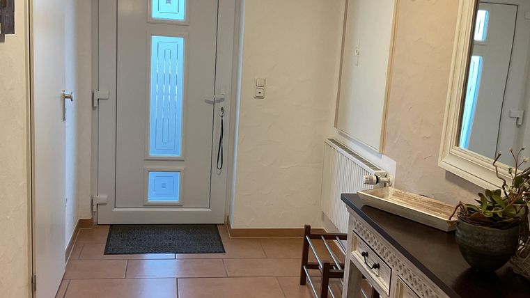 A bright hallway with a white front door and a large mirror. There is a practical console with decor and a small stool.