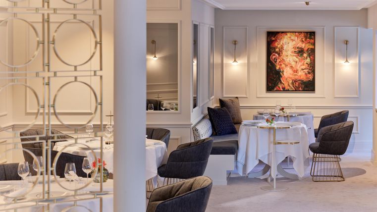 An elegant restaurant with stylish tables and cozy armchairs. A modern artwork hangs on the wall.