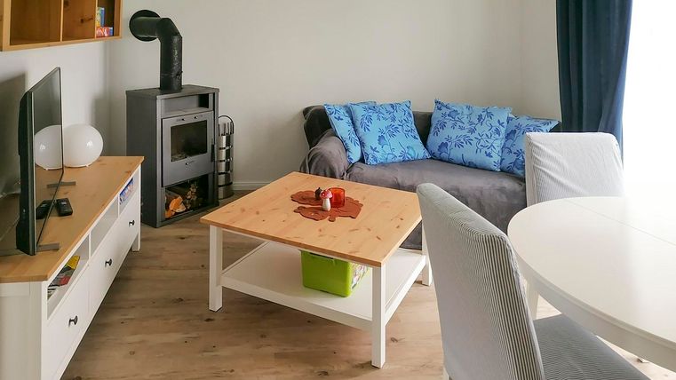 Een gezellige woonkamer met een moderne bank en blauwe kussens. De houtkachel en de tafel zijn centrale elementen van de ruimte.