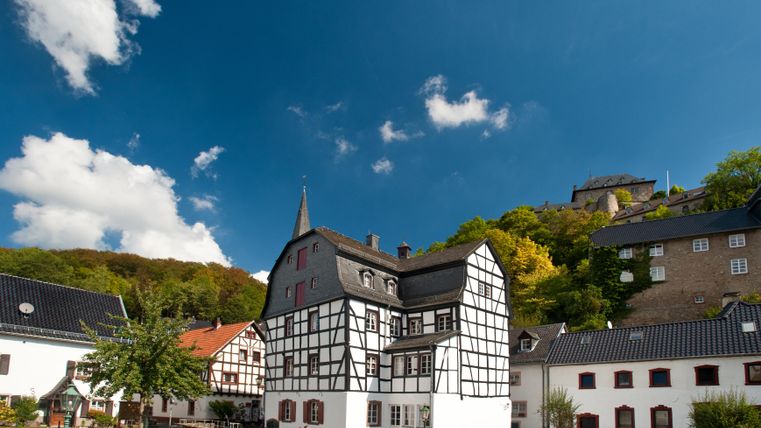 Ein malerisches Dorf mit Fachwerkhäusern und grünen Hügeln im Hintergrund. Der Himmel ist klar und blau, ideal für einen entspannten Tag.