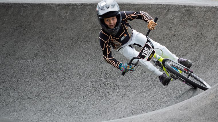 A young BMX rider speeds through a winding course. He is wearing a helmet and special cycling clothing.