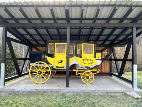 Eine historische Kutsche in einem überdachten Stall. Die Kutsche ist gelb und schwarz mit auffälligen Rädern.