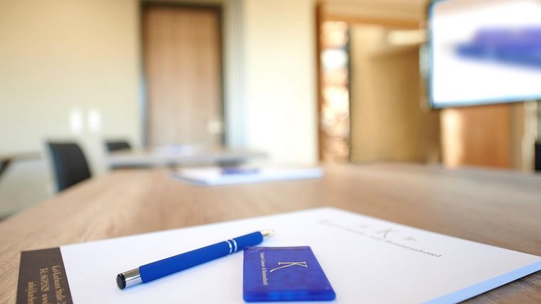 Ein Tisch in einem Konferenzraum mit einem blauen Stift und einem Informationsblatt. Im Hintergrund ist ein Bildschirm sichtbar.