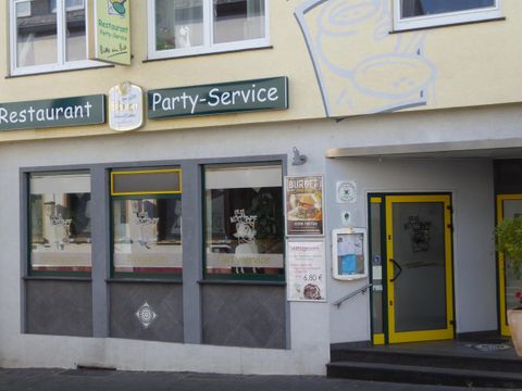 Ein Restaurant mit einer schlichten Fassade und einem Party-Service. Die Fenster zeigen eine freundliche Atmosphäre und das Eingangstor ist gut sichtbar.