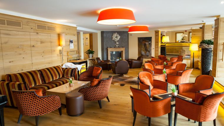 Eine gemütliche Lobby mit roten Stühlen und einer modernen Couch. Das warme Holzdesign schafft eine einladende Atmosphäre.