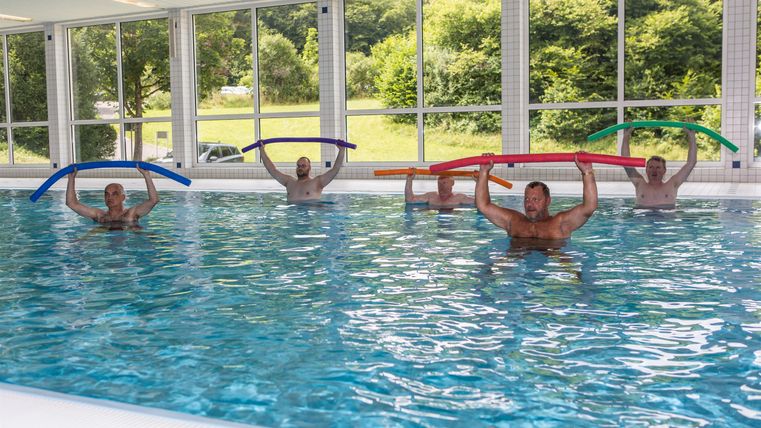 Een groep mensen doet aquafitness in het zwembad. Ze houden kleurrijke zwemnoedels vast en oefenen samen.