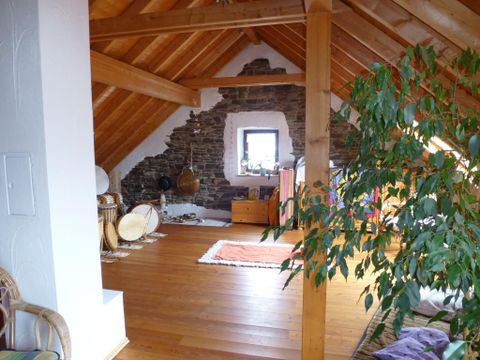 Een gezellige zolderkamer met houten balken en een mooi uitzicht op de natuur. In de kamer bevinden zich planten en traditionele muziekinstrumenten.