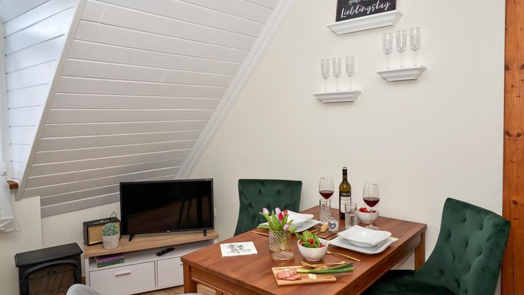 A cozy dining area with a table, two chairs, and a TV corner. On the table are wine and fresh flowers.