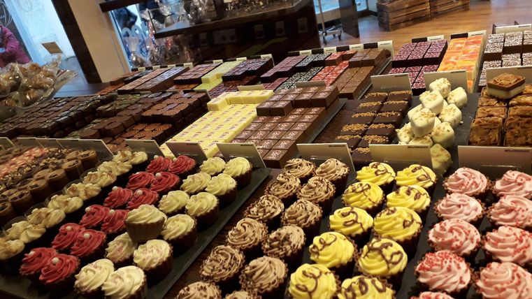 Eine Vielzahl von bunten Cupcakes und Schokoladenleckereien ist in einem Geschäft angeordnet. Die Auswahl umfasst verschiedene Farben und Toppings.