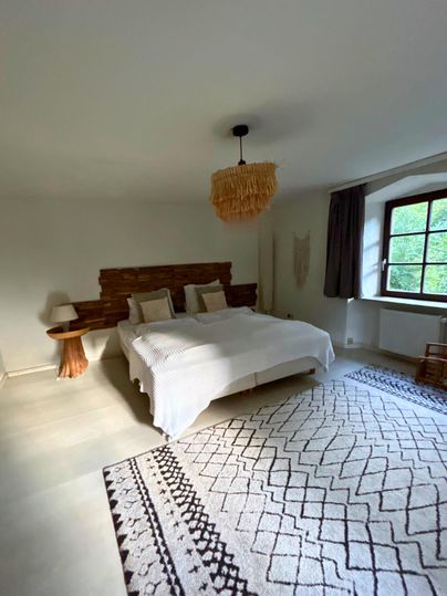 A bright bedroom with a large bed and natural wood. A cozy rug and a window create an inviting atmosphere.