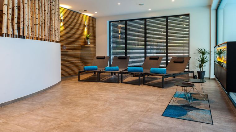 Ein modernes Entspannungszimmer mit Liegen und großen Fenstern. Die Atmosphäre ist ruhig und einladend, ideal zum Ausruhen.