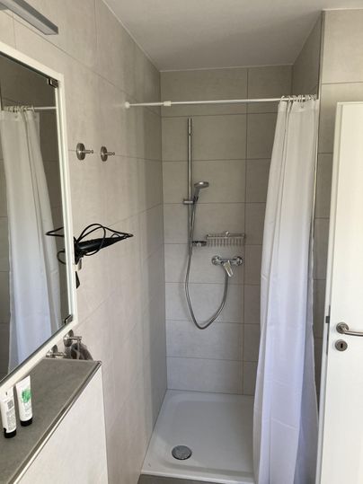 Ein modernes Badezimmer mit einer Duschkabine und einer weißen Duschvorhang. Die Wände sind hell und fliesenartig gestaltet.