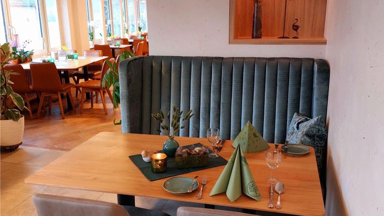 Ein gemütlicher Tisch in einem modernen Restaurant, umgeben von grünen Pflanzen. Die Tischdeko besteht aus grünen Servietten und Kerzen.