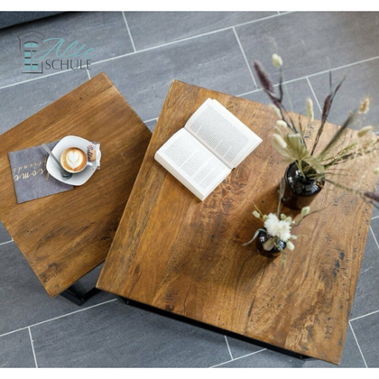 Ein eleganter Holztisch mit einer offenen Buchseite und einer Blumenvase. Neben dem Tisch steht eine Tasse Kaffee auf einem Untersetzer.