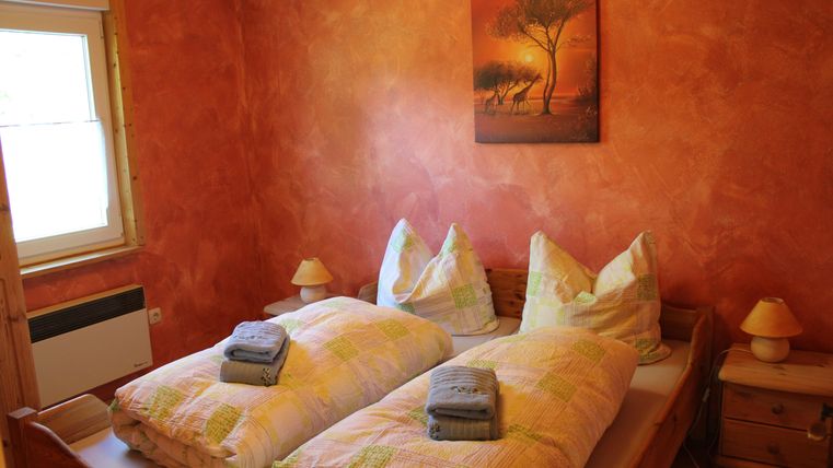 Een gezellige slaapkamer met twee bedden, die zijn versierd met kleurrijke dekens en handdoeken. De muren zijn geschilderd in warme oranjetinten en een schilderij van een boom hangt boven het bed.