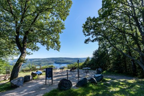Ein Aussichtspunkt mit Blick auf einen See, umgeben von Bäumen. Der Himmel ist klar und der Bereich ist mit Steinen und Pfaden gestaltet.