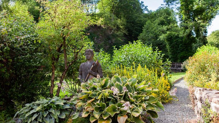 Ein schöner Garten mit verschiedenen Pflanzen und Sträuchern. In der Mitte steht eine Statue inmitten der grünen Umgebung.