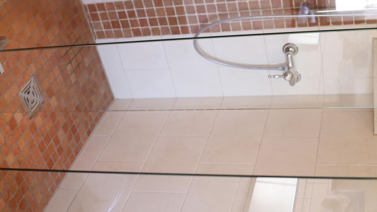 Eine moderne Duschkabine mit einer Glaswand und einer Regenbrause. Der Boden ist mit braunen Fliesen gestaltet.