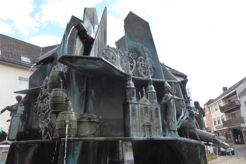 An artistic fountain with various sculptures depicting dynamic figures. The bronze surface reflects light and creates an interesting play of shadows and form.