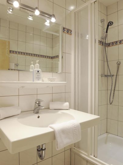 Ein modernes Badezimmer mit einer Dusche und einem Waschbecken. Helle Fliesen und eine Spiegelbeleuchtung sorgen für eine einladende Atmosphäre.