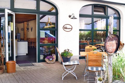 Ein einladendes Restaurant mit großen Fenstern und einem gemütlichen Außenbereich. Vor der Tür stehen Tische und Stühle, die zu einer entspannten Mahlzeit einladen.