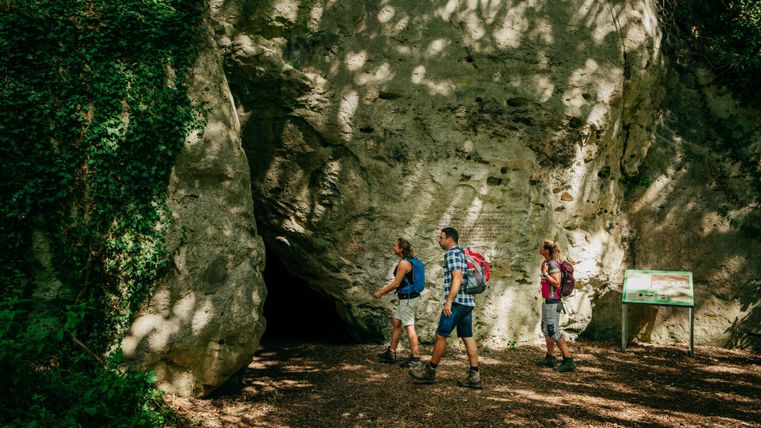 A group of hikers passes by a large rock. In the background, a directional sign can be seen.
