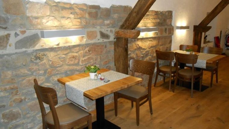 Cozy restaurant with wooden tables, chairs, and stone wall. Subtle lighting and plants create an inviting atmosphere.