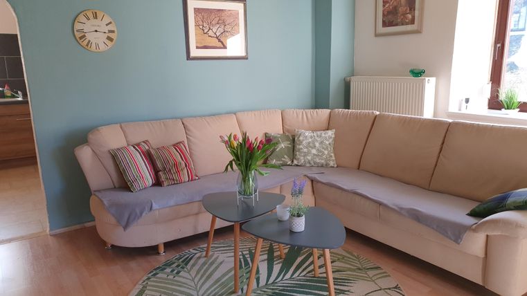 Een gezellige woonkamer met een beige bank en een moderne tafel. Aan de muur hangen schilderijen, en verse bloemen sieren de tafel.