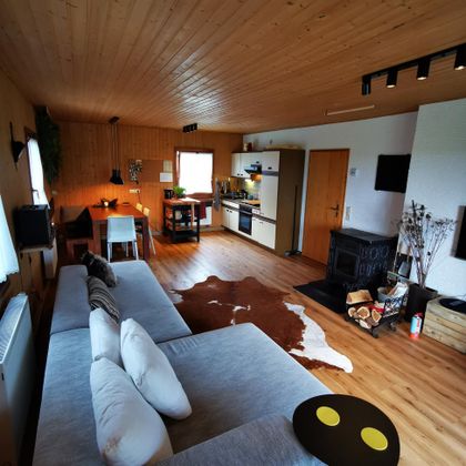 Een gezellige woonkamer met houten plafonds en een grote bank. De inrichting is modern en uitnodigend, met een eetgedeelte en een keuken.