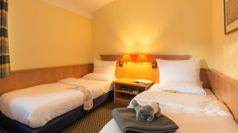 Ein gemütliches Hotelzimmer mit zwei Einzelbetten. Es ist hell und freundlich, mit einer warmen Farbgebung.